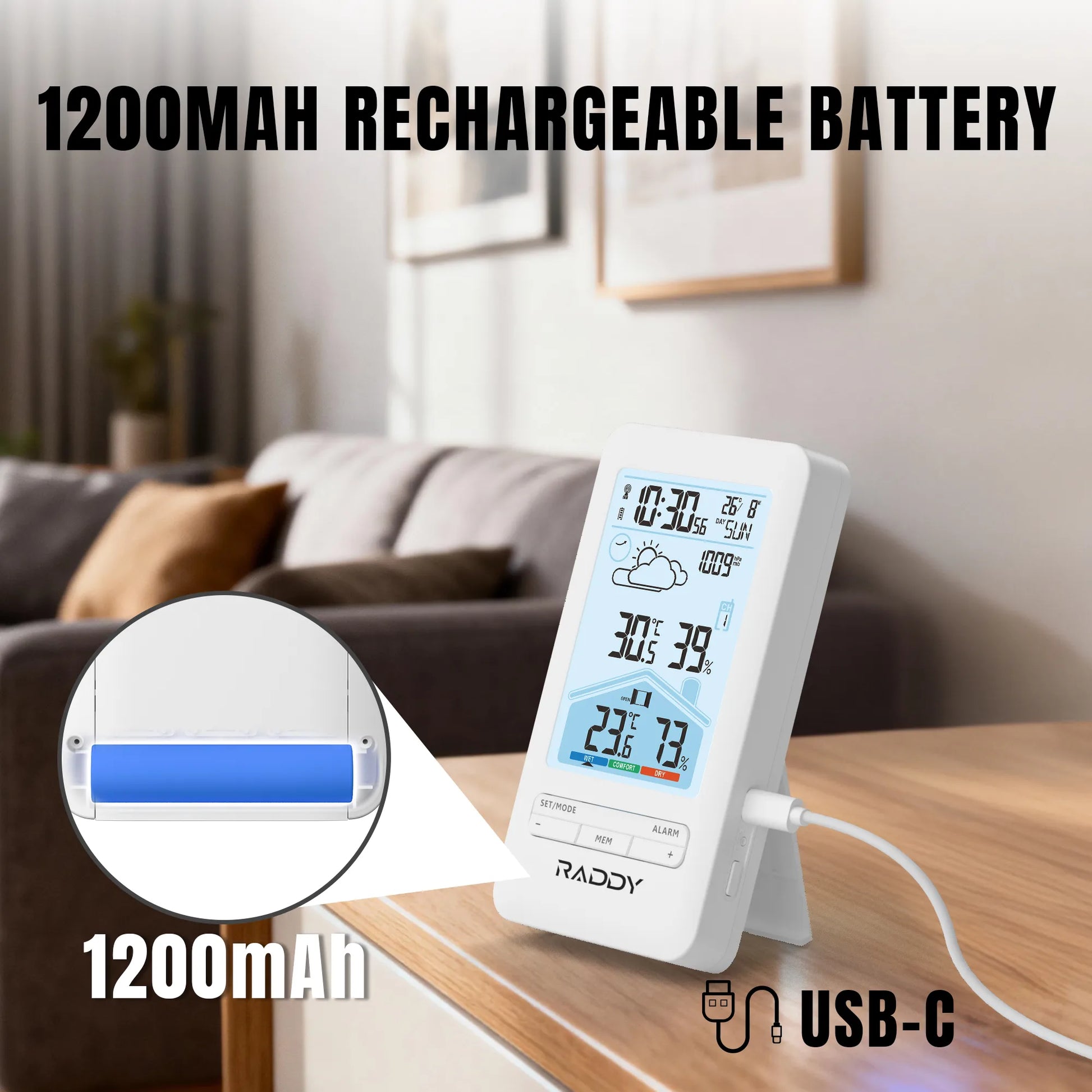 Digital clock with weather display on a table in a living room, featuring a 1200mAh rechargeable battery.